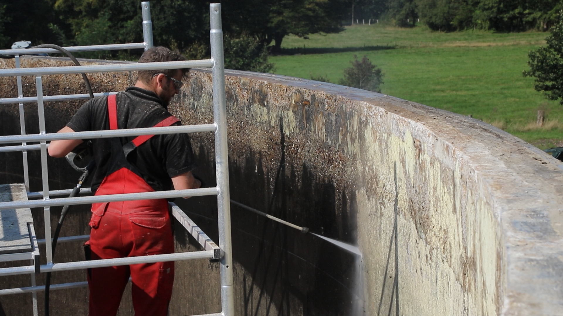Arbeiter auf einer Leiter reinigt einen großen Behälter mit Hochdruckwasser